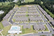 Scenic aerial view of a sprawling apartment community with neatly arranged buildings, ample parking, and lush green surroundings, featuring a luxurious pool area for residents.