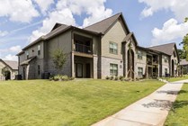 Charming modern apartment community with lush green lawns and picturesque palm trees under a bright blue sky.