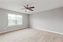 Bright, spacious bedroom with a modern ceiling fan and plush carpeting, featuring a large window with blinds for natural light.