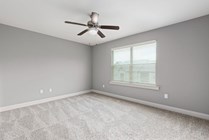 Bright and airy bedroom room with plush carpet, large window, and modern ceiling fan.
