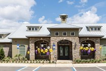 Charming residential building with elegant stone facade and inviting entrance, adorned with colorful balloons, surrounded by lush landscaping under a vibrant blue sky.