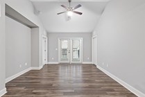 Bright and spacious living area with elegant wooden flooring, modern ceiling fan, and double doors leading to a balcony.