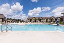 Inviting, large sparkling pool, surrounded by comfortable lounge chairs and framed by a beautiful blue sky.